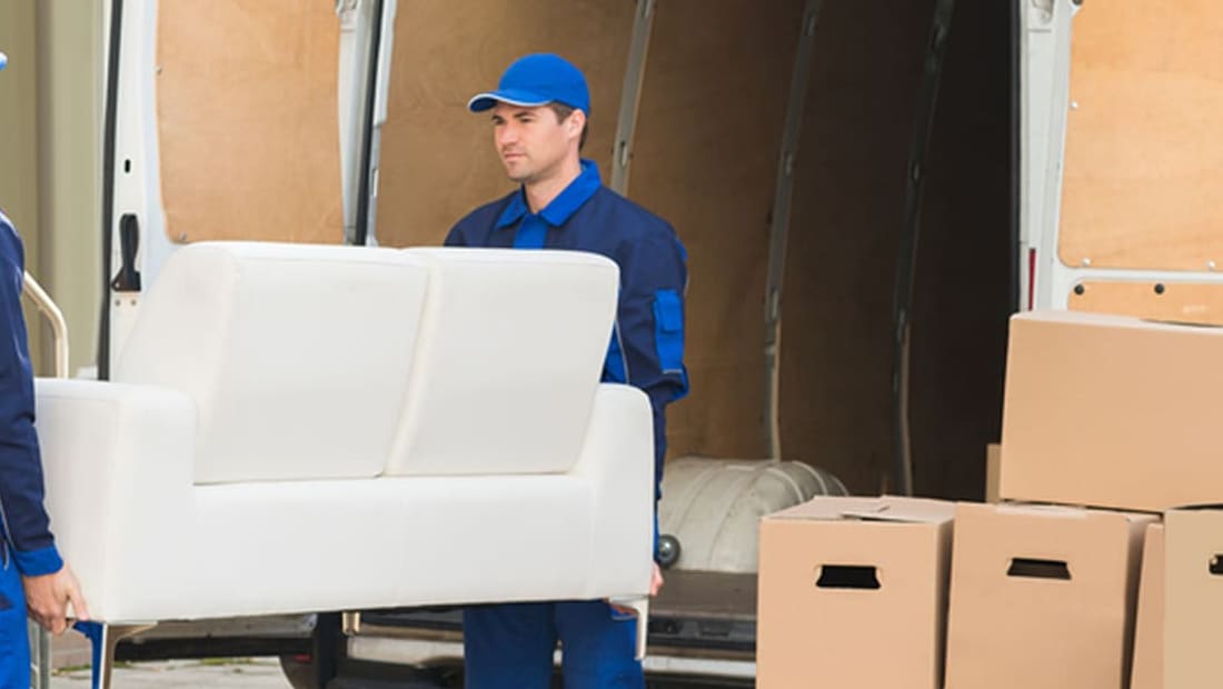 Movers loading a white loveseat and packed boxes into a moving truck